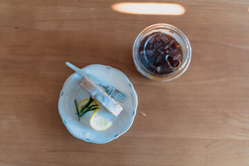 A slice of lemon cake and iced Americano on wood background.