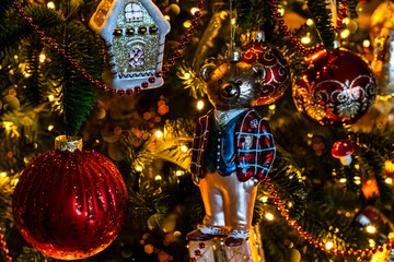 Christmas tree with red balls, gingerbread house and teddy bear decorations, selective focus. A Christmas background with festive lights and beautiful glitter bokeh