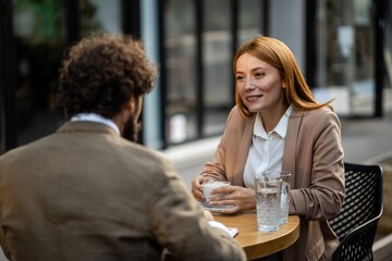 Businesswoman smiling and drinking coffee at outdoor cafe meeting with businessman