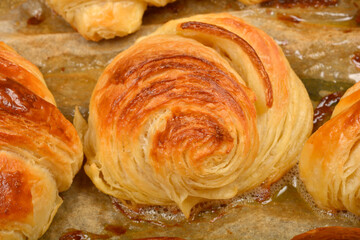 A detailed close-up of a freshly baked, golden-brown spiral pastry with a glossy sheen on a baking sheet