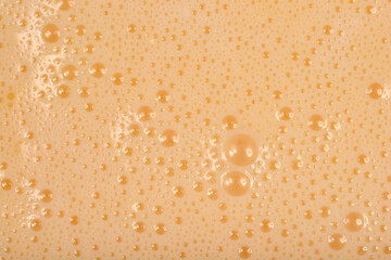 A full-frame, close-up shot captures the texture of a smooth, light beige liquid batter covered in tiny foam bubbles.