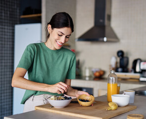 Portrait of a young woman preparing and eating breakfast, drinking juice in the kitchen at home