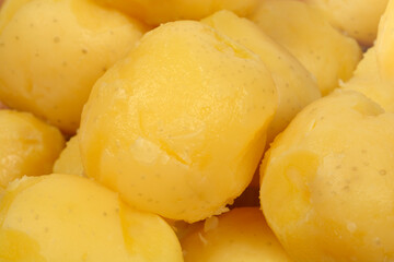 A close-up, high-angle shot shows a dense pile of smooth, golden-yellow peeled boiled potatoes filling the frame