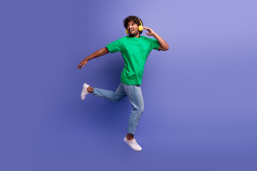 Fototapeta premium Energetic young man enjoying music with headphones while posing playfully on a vibrant purple background