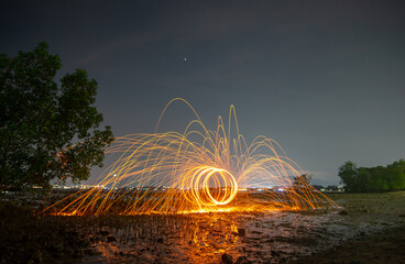 reflection of spark fire swirl from steel wool with long exposure speed motion abstract at twilight on the sea. 
Sparks of light bounces off the water in reflected lines.
dark sky background.