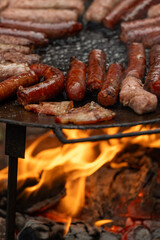 A large, round, flat metal grill, discada or plow disc grill, being used over an open flame. Sausages, pork and beef steaks, and kebabs are cooked on it. A little greenery is visible in the background