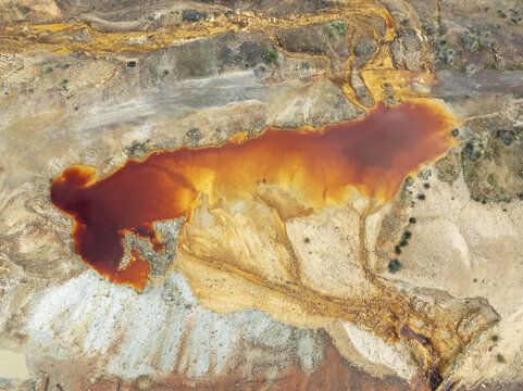 Aerial view of a vibrant, rust-colored pond, a striking contrast of textures and tones in the mineral-rich ground in Minas de Riotinto, Andalusia, Spain.