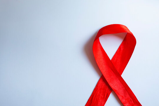 A red fabric ribbon on a white background is a symbol of the fight against cancer.