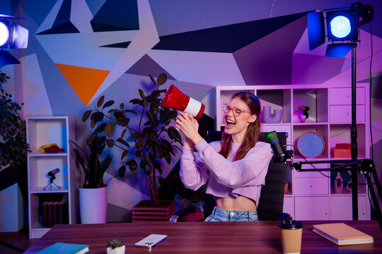 Young female vlogger creating engaging content with a megaphone in a vibrant studio lit with colorful neon lighting