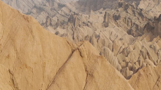 Aerial view of the stark, eroded landscape of Hongshan Stone Forest, showcasing the varied textures and tones of the arid terrain, Kuqe, Xinjiang, China.