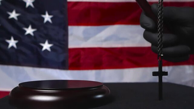 Wooden brown court hammer slammed on a wooden pad by a court justice with a holy cross hangin in the foreground and United States of America flag in the bokeh blurry background. Slow motion movement.