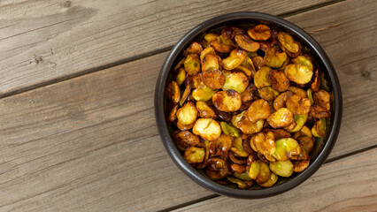 Top view of homemade roasted broad beans(Vicia faba) in a bowl on rustic wooden table with space for text or logo.