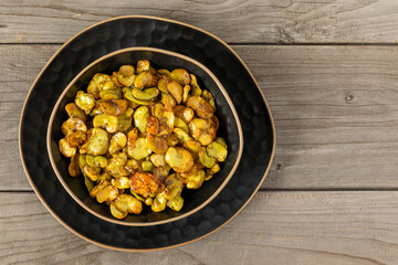 Lightly toasted fava beans (Vicia faba) in a bowl on a rustic wooden table with copy space.