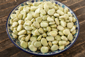 Raw fava beans (Vicia faba) with the second skin on a platter. Rustic wooden background.