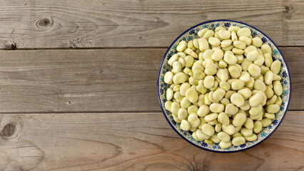Raw broad beans (Vicia faba) with the second skin on a hand colored platter. Rustic wooden background with space for text or logo.