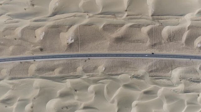 Aerial view of a road cutting through sand dunes, with vehicles contrasting against the vast desert landscape, Taklamakan Desert, China.