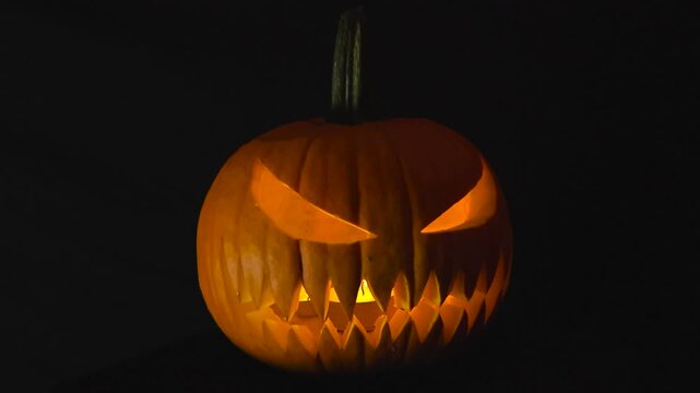 Orange carved Halloween pumpking with candles burning inside of it placed in front of a black studio background. Scary eyes and mouth with sharp teeth. Jack o lantern trick or treating pumpkin.