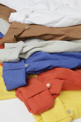 Colorful linen shirts stacked on a white surface.