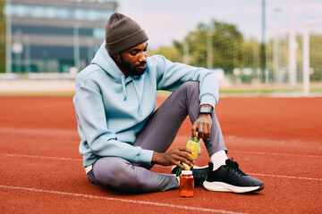 Black man resting on running track taking supplements