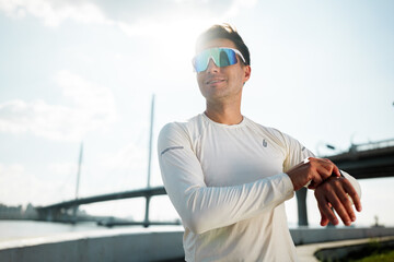 Man in sportswear adjusting smartwatch near river in urban setting