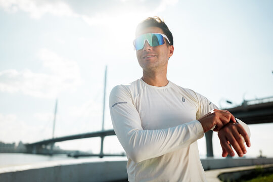 Man in sportswear adjusting smartwatch near river in urban setting