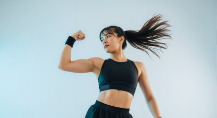 Athletic Asian woman flexing her bicep. Strong female athlete in sportswear showing her muscles. Fitness, power, and workout motivation concept