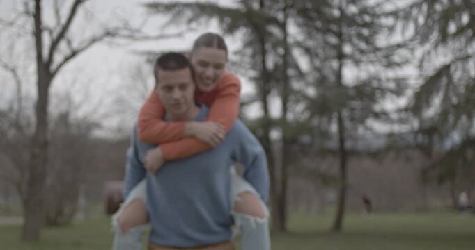 A happy young couple shares a joyful moment in a lush green park. The man gives the woman a playful piggyback ride, showcasing their strong bond and carefree happiness outdoors.