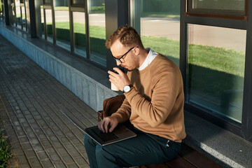 Young university teacher enjoying coffee while working on laptop outside campus
