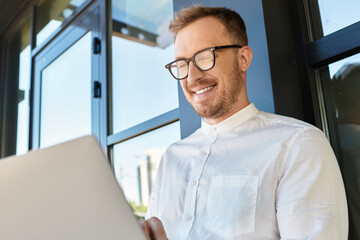 Fototapeta premium Young university teacher enjoys a sunny day while working on his laptop outdoors