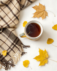 Cozy composition in flat lay style, golden autumn. A cup of steaming tea, a soft blanket and scattered yellow leaves