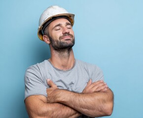 A relaxed construction worker in a light gray shirt poses against a light blue backdrop, wearing a protective helmet.