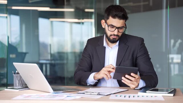 Busy businessman making financial calculations using calculator and laptop taking notes sitting at desk at workplace in business office. Financier working, fills out documents or engaged in accounting
