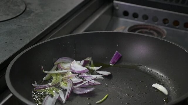Close-up of a cook saut&eacute;ing julienned red onions in a hot Teflon pan with olive oil.