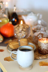Lit candles, cookies, chocolate, nuts, tea, wine, pumpkins, books, reading glasses and autumn leaves on the table. Autumnal hygge at home. Selective focus.