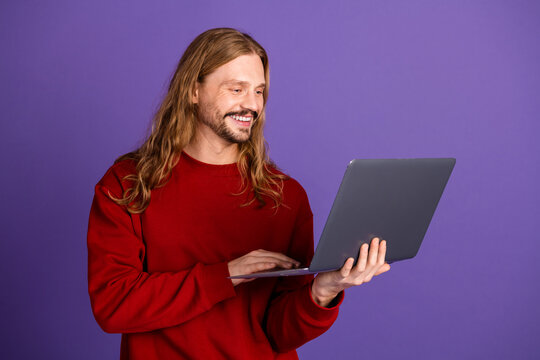Young man with long hair using laptop against purple background in casual stylish fashion