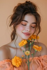 Fototapeta premium A young woman with long hair smiles gently while holding bright yellow flowers near her face. She stands in front of a peach-colored background, capturing the essence of spring in a warm setting