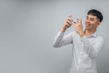 A handsome young Asian man smiles happily while using a social media or gaming app on a modern smartphone. This concept is ideal for technology, connectivity, lifestyle, and leisure.

