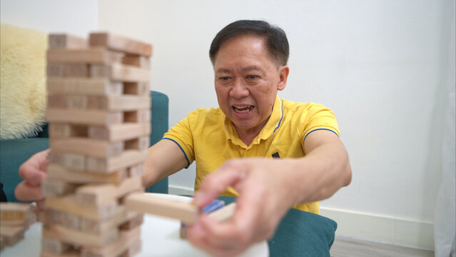 On a holiday, an elderly man enjoys a jenga game in living room of house