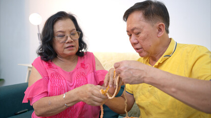 Senior woman knitting colorful yarn and tries to teach her husband how to knit on the sofa