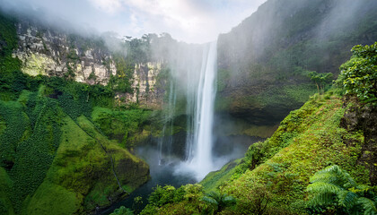 Fototapeta premium A Large Majestic Waterfall Cascades Over Cliffs Creating Mist That Envelops The Lush Greenery Below In A Serene Natural