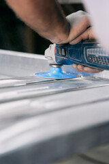 Close up of workers hand operating an angle grinder with blue disc to polish and smooth metal surface in industrial workshop.