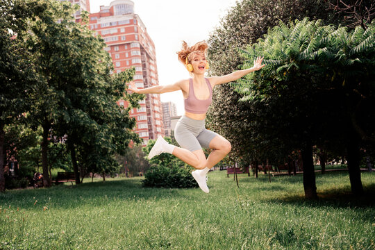 Joyful athlete in sportswear jumping in the park on a sunny day, practicing fitness in an urban outdoor environment