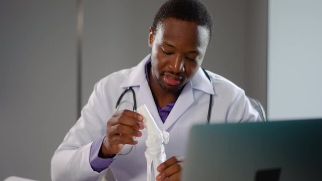 African male doctor conducts a telemedicine online webcam video call session and And there is a bone model with care instructions with a patient, demonstrating the importance of remote healthcare. 