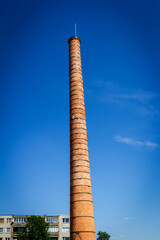 Fototapeta premium Old tall factory chimney made of bricks against blue sky.