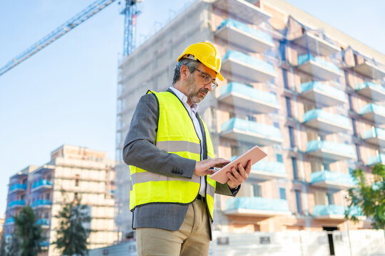 Construction engineer analyzing plans using digital tablet at building site