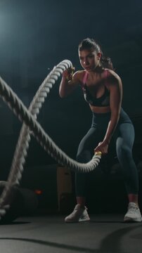 Strong woman exercising with battle ropes in gym angle view focus endurance discipline strength training healthy lifestyle motivation concept vertical slow motion fitness workout