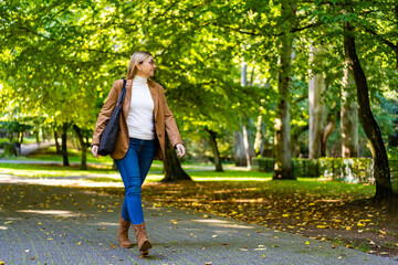 Beautiful middle aged woman walking in city park on early autumn day. Front view	
