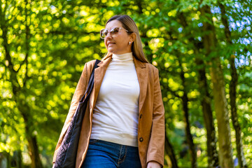 Beautiful middle aged woman walking in city park on early autumn day. Front view	