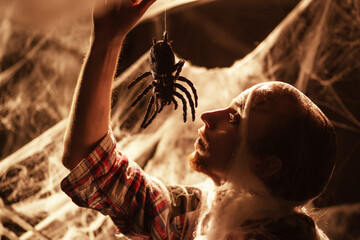 Sinister man eating big spider, trying to scare. Dead guy against black background in spiderwebs