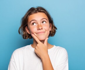 A thoughtful young girl gazes upwards, lost in contemplation, against a vibrant light blue backdrop.